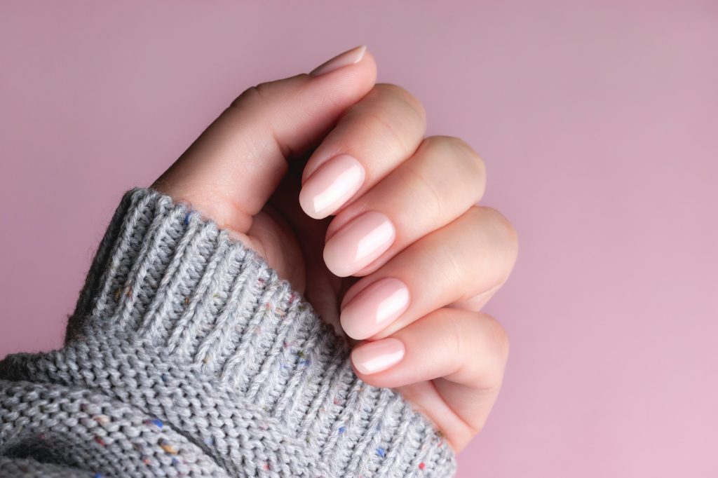 Hand in sweater with nude nails on pink background