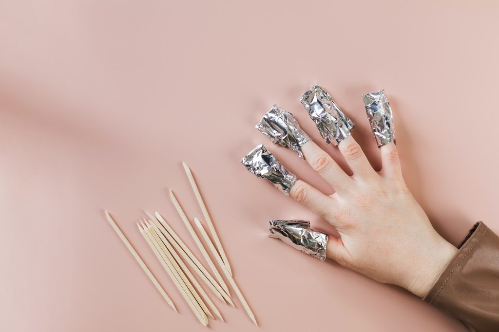 The process of removing gel polish from nails. Nails are wrapped in falga on a pink background.